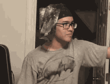 a man wearing glasses and a batman shirt stands in a doorway
