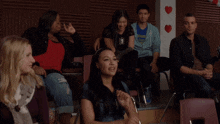 a group of people are sitting in chairs in front of a wall with red hearts on it