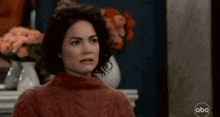 a woman in a red sweater is making a funny face while sitting in front of a fireplace .