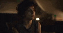 a young man with curly hair is sitting in a dark room with his eyes closed and a necklace around his neck .