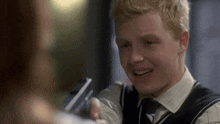 a young man in a vest and tie smiles while talking to a woman