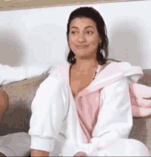 a woman in a pink robe is sitting on a couch with her legs crossed .