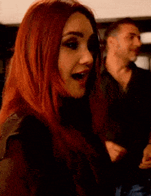 a woman with red hair has her mouth open and a man in the background