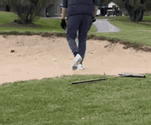 a man is walking on a golf course with a rake in the grass .