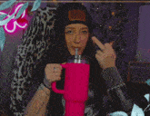 a woman in a black hat holds a pink mug and shows the middle finger