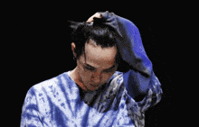 a man wearing a blue tie dye shirt holds his hand to his forehead