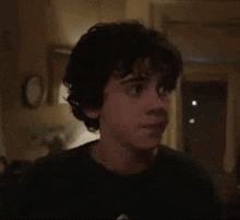 a young boy with curly hair is standing in a dark room making a funny face .