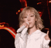 a woman with blonde hair and glasses is singing into a microphone .