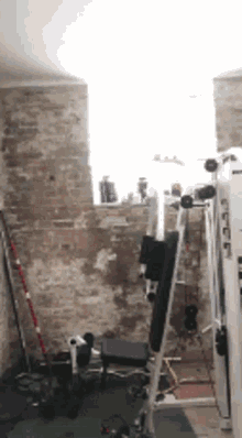 a gym with a brick wall , a bench , a machine and a window .