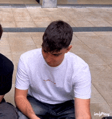 a man wearing a white t-shirt that says " the greatest is yet to come " is sitting on the ground