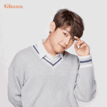 a young man wearing a grey sweater and a white shirt has his hands folded in front of his face