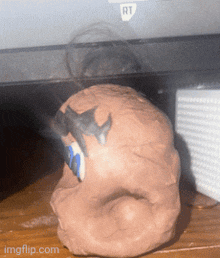 a piece of clay with a shark on it sits on a wooden table next to a computer monitor that says rt