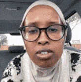 a woman wearing glasses and a head scarf is sitting in a car .