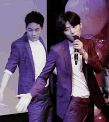 a man in a suit is holding a microphone while another man stands behind him