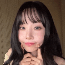 a woman with long black hair and bangs is making a funny face with her hands on her face .
