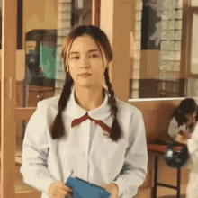 a girl in a school uniform with pigtails is standing in a classroom holding a purse .