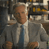 a man in a suit and tie is sitting at a table with countdown written on the bottom of the image