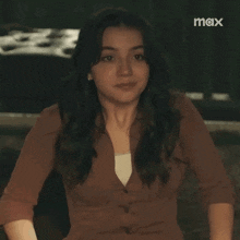 a woman in a brown shirt is sitting in a dark room and looking at the camera .