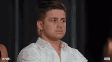 a man in a white shirt is sitting with his arms crossed and # mafs written on the bottom