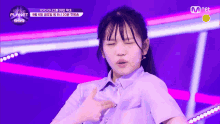 a girl in a purple shirt is pointing at her chest with a mnet logo behind her