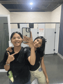 two girls taking a selfie in a bathroom with a sign on the wall that says no smoking