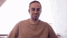 a man wearing glasses and a gold chain looks at the camera ..