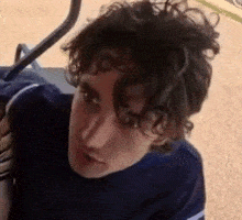 a young man with curly hair is sitting in a golf cart looking at the camera .