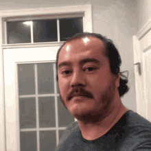 a man with a mustache is taking a selfie in front of a window
