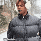 a man wearing bunny ear muffs and a black jacket has a tiktok sticker on his jacket