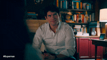 a man in a white shirt is sitting in front of a bookshelf with the hashtag #superman on the bottom
