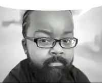 a man with a beard wearing glasses looks at the camera