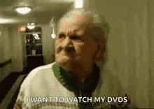 an elderly woman is standing in a hallway and talking about watching her dvds .