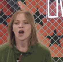 a woman in a green shirt stands in front of a chain link fence with the letter u on it