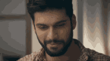 a man with a beard wearing a plaid shirt looks down