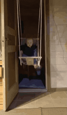 a baby is sitting on a wooden swing in a doorway