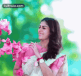 a woman in a white saree is smiling and holding pink flowers .