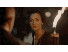 a woman is looking at a man in the dark with a torch in the foreground .