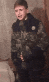 a young boy in a camouflage jacket is standing in a room with his mouth open .