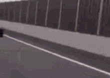 a black car is driving down a highway next to a fence .