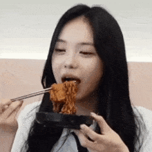 a woman is eating noodles with chopsticks from a black bowl .
