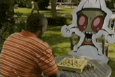 a man is sitting at a table playing chess with a cardboard cutout of a monster .