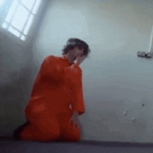 a man in an orange jumpsuit is kneeling on the floor in a cell .