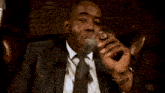 a man in a suit and tie is smoking a cigar while sitting in a leather chair .