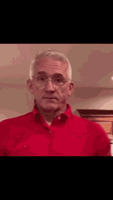 a man in a red shirt and glasses is looking at the camera .