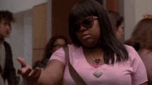 a woman wearing sunglasses and a pink shirt has a heart shaped necklace