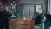 a man in a suit is sitting at a desk talking to another man in a chair .
