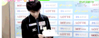 a man holding a cake in front of a wall with lots of logos for lotte