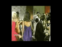 a woman in a purple dress is dancing with a man in a suit in front of a crowd with the number xxx on the bottom