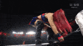 a woman with red hair is kneeling down in a wrestling ring with the letters w on the bottom right