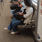 a woman sits on a subway seat looking at her phone